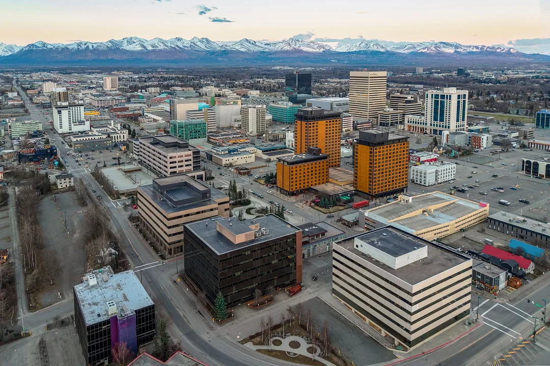 Aerial view of city blocks in Alaska with snow-covered mountains on the horizon.