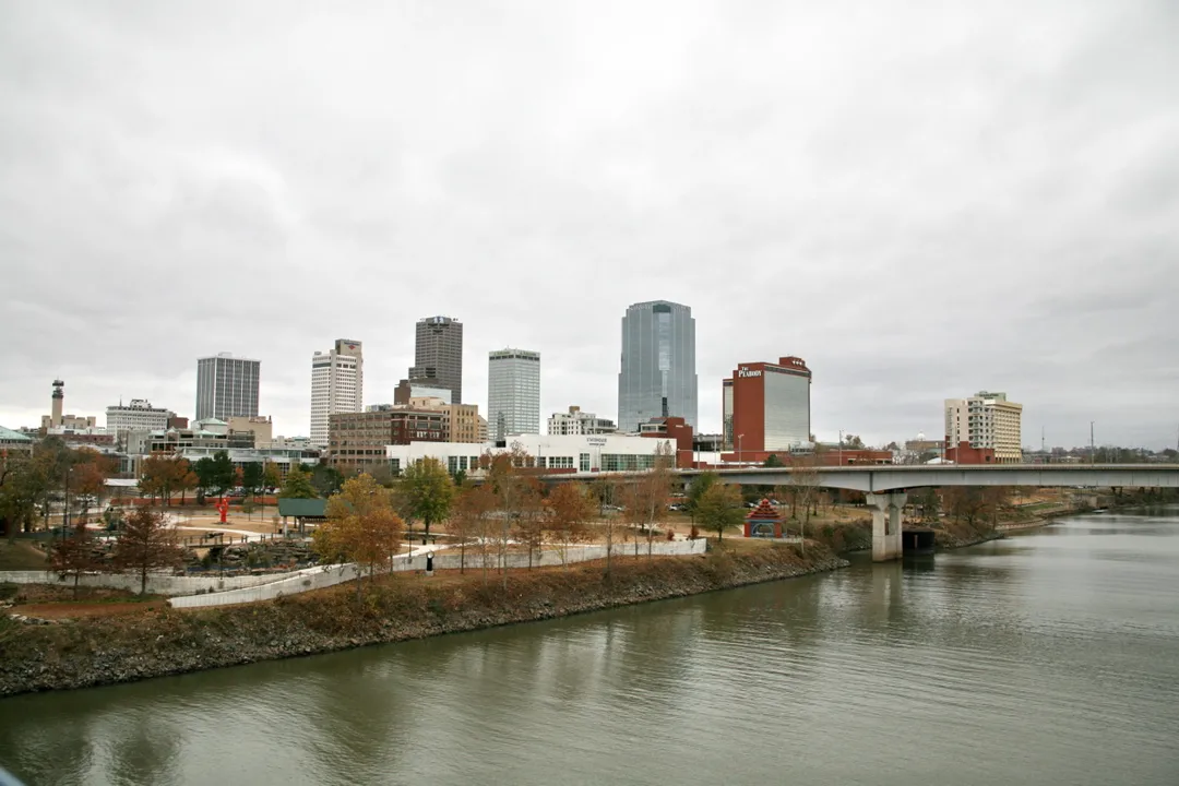 A bridge crosses a river beneath a cluster of downtown towers in Arkansas.