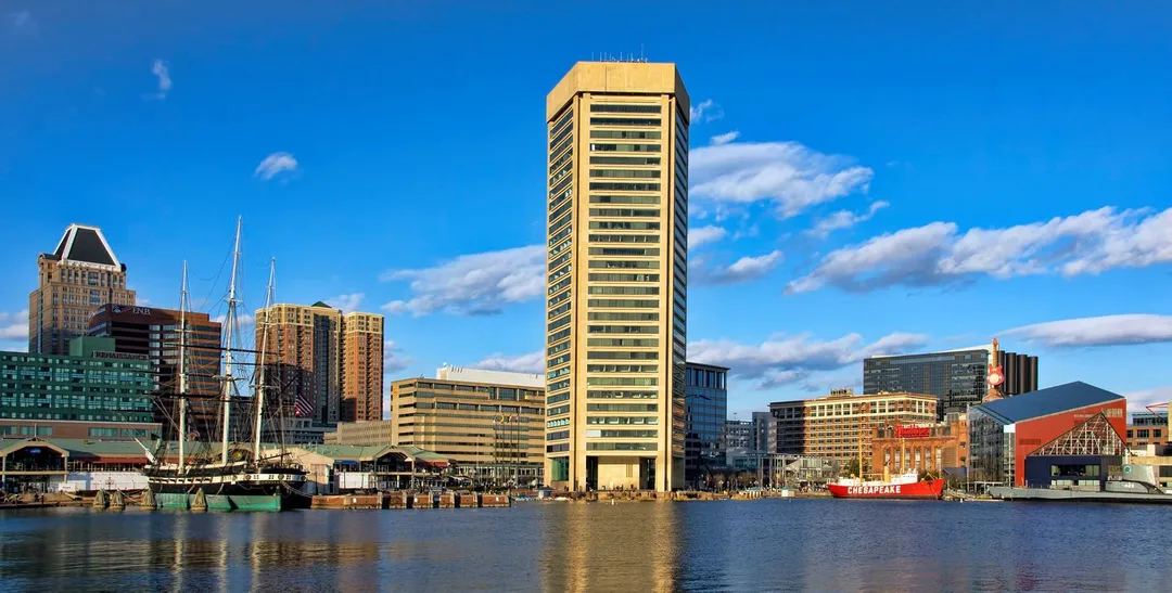 A tall golden-colored tower and waterfront buildings beside a Maryland harbor.